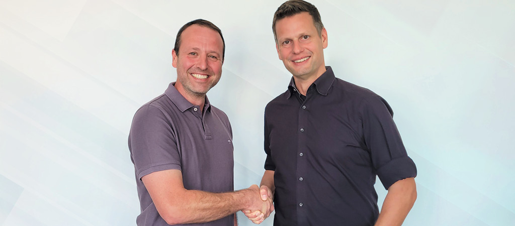 Two people smile into the camera and shake hands
