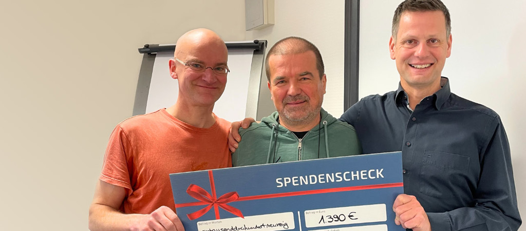 Three people with a check in their hands smile at the camera