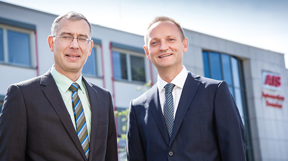 Zwei Personen in Anzügen stehen vor einem Gebäude