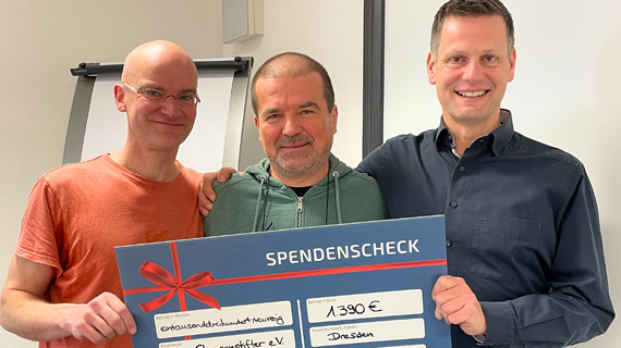 Drei Personen halten einen Scheck in der Hand